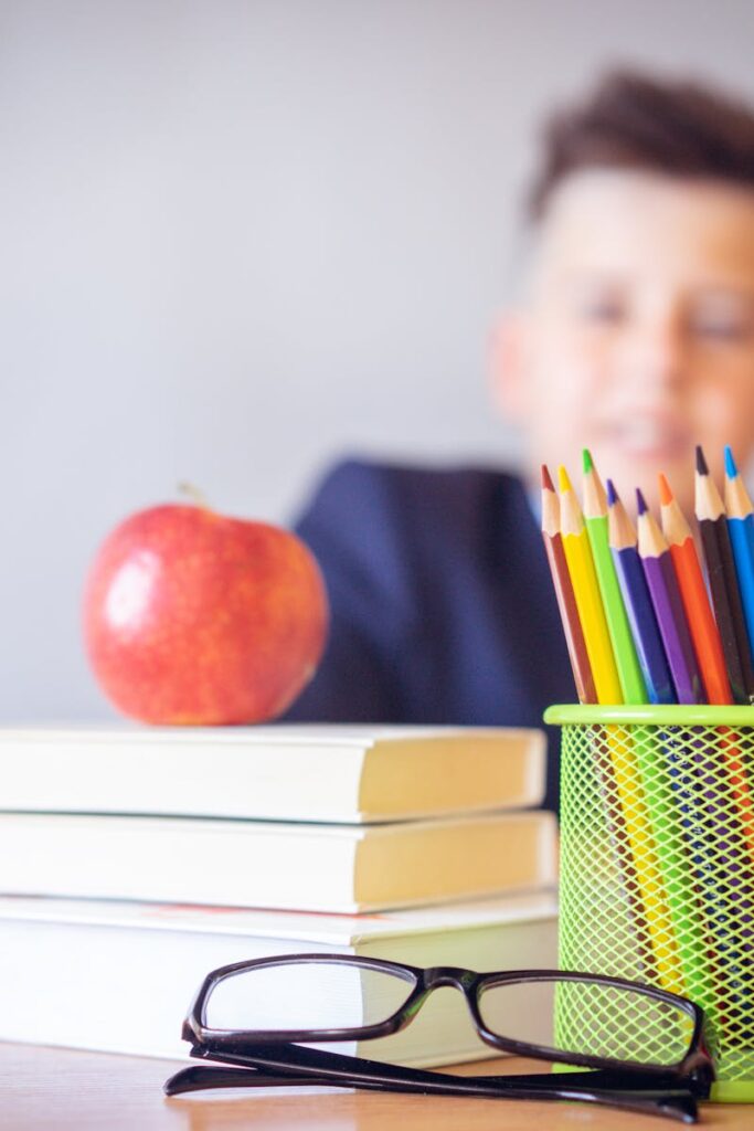 Schoolboy smiling behind a desk with books, pencils, and an alarm clock symbolizing study and creativity.